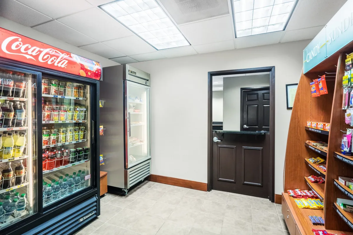 A bright, casual interior spot showcasing a Coca-Cola vending machine, a refrigerated unit, and a snack display. The space exudes a welcoming, everyday vibe, perfect for guests grabbing a quick bite or drink.