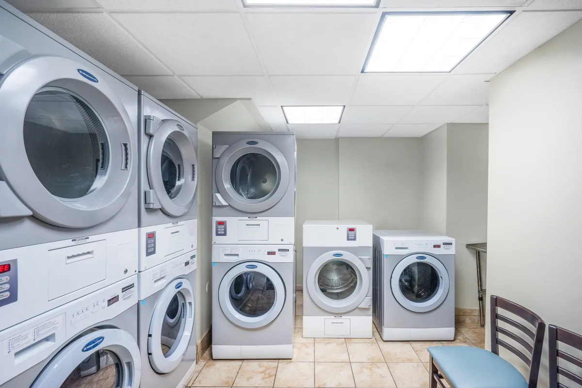 This image depicts a practical laundry room featuring stacked washers and dryers with a single chair and a utility table. The scene is clean and efficient, emphasizing accessible laundry facilities for guests.