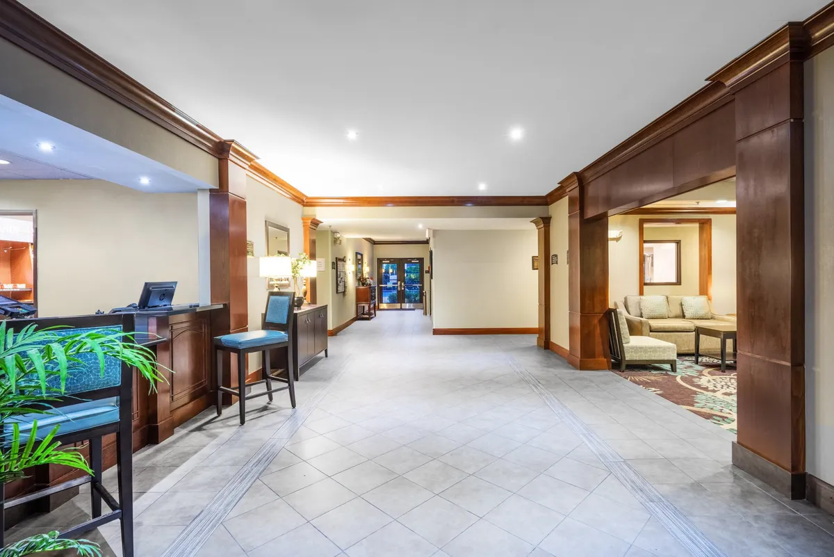 A modern interior with a reception desk and adjacent seating area, accented by decorative plants. The open layout encourages socializing and provides a relaxed environment for gathering before meals or receptions.