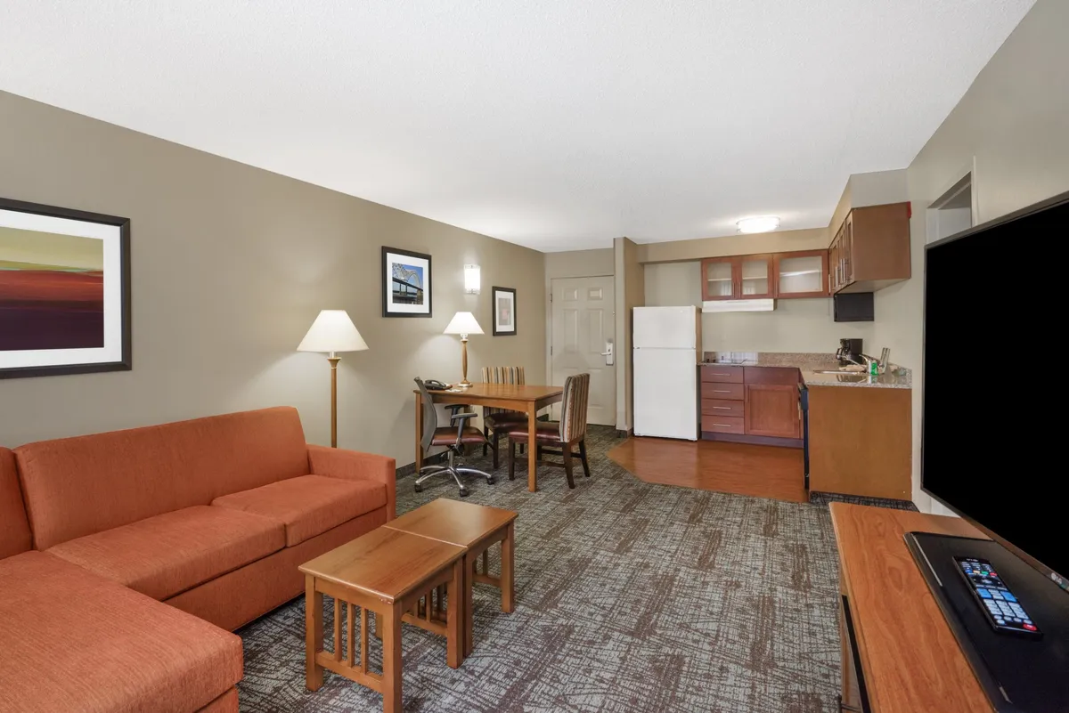 The hero image captures a bright, inviting open-concept living area with a modern orange sofa, a cozy dining table set for meals, a fully equipped kitchen area, and vibrant artwork adorning the walls. The scene exudes warmth and comfort, making it easy to imagine relaxing, sharing meals, or enjoying downtime after exploring Memphis.