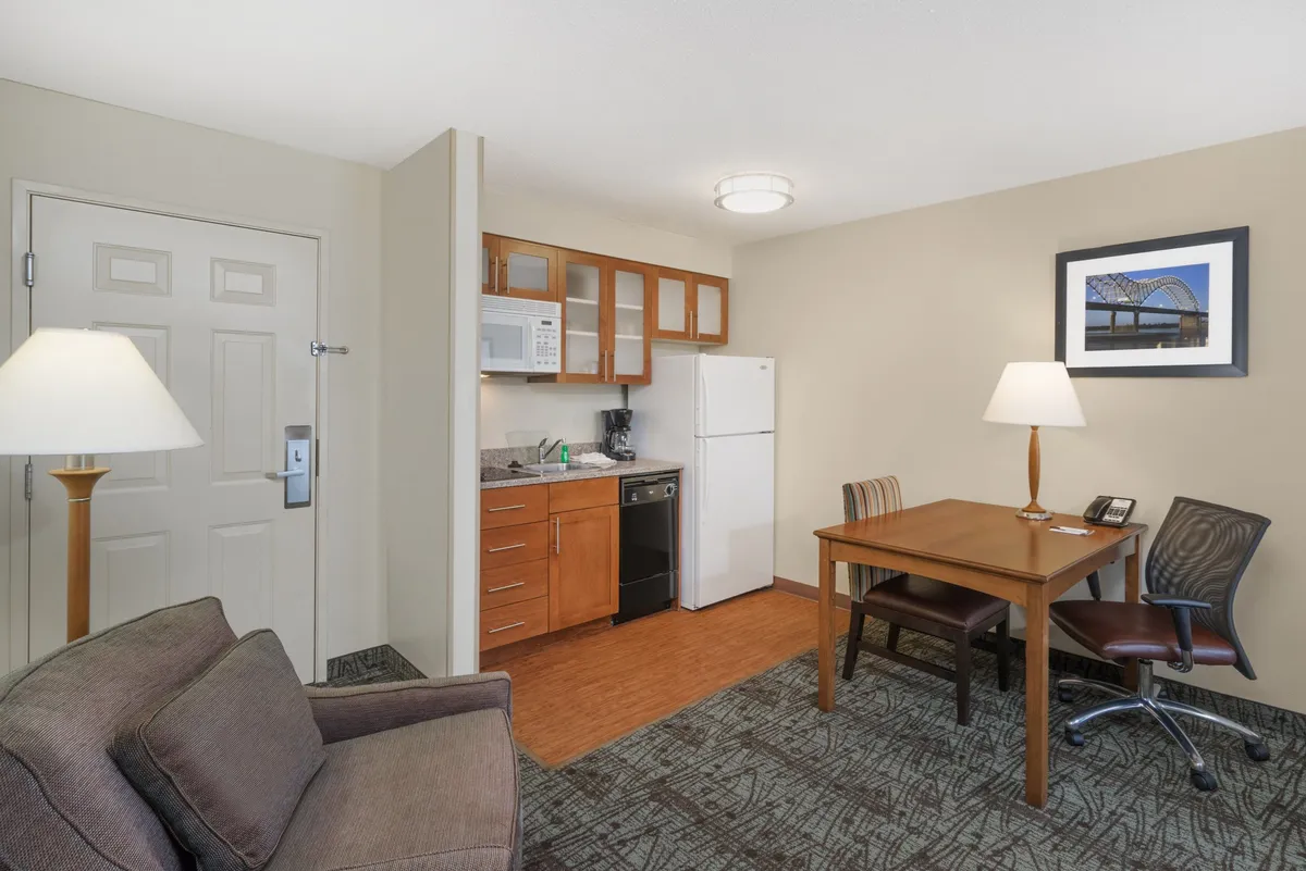 This image captures a cozy interior scene featuring a kitchenette, a dining table, a comfortable sofa, and a standing lamp. The space feels inviting and homelike, with natural light enhancing the ambiance. It highlights the central living area where guests can relax, dine, or unwind after a busy day.